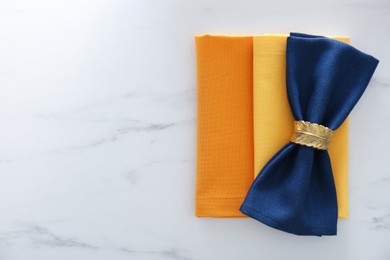 Photo of Colorful napkins and decorative ring on white marble table, top view. Space for text