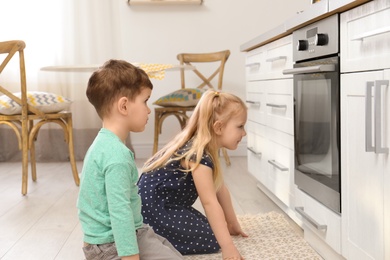Photo of Cute children sitting near oven in kitchen