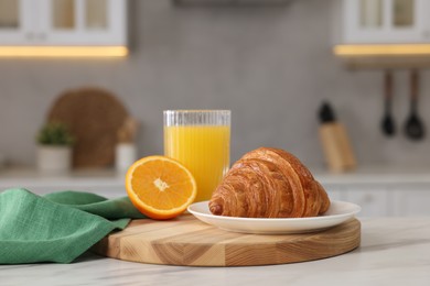 Breakfast served in kitchen. Fresh croissant and orange juice on white table