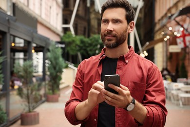 Handsome man using smartphone on city street, space for text