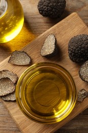 Photo of Glass bowl of truffle oil with wooden board on table, flat lay