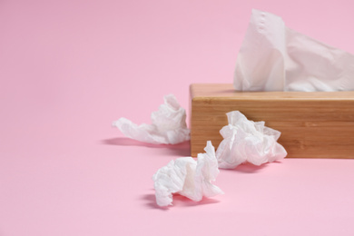 Holder with paper tissues and used crumpled napkins on pink background