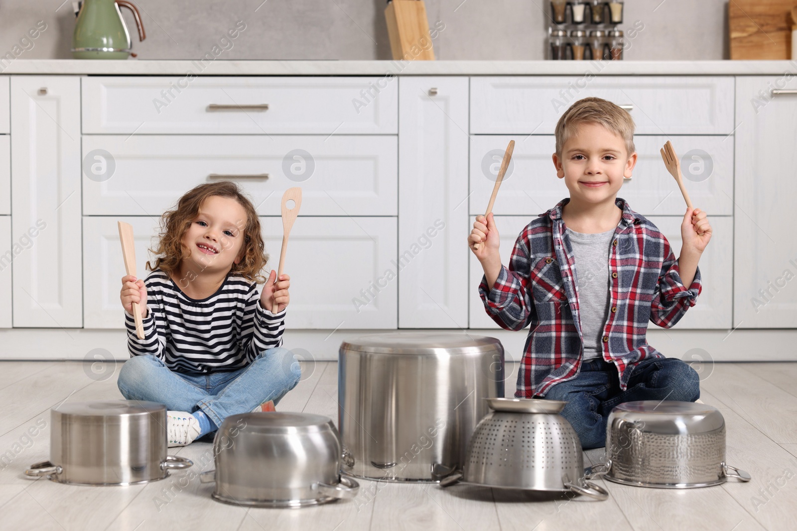 Photo of Little children pretending to play drums on pots in kitchen