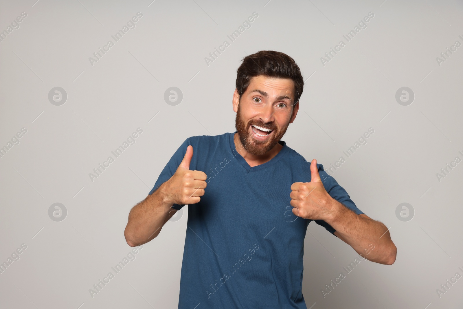 Photo of Handsome bearded man showing thumbs up on light grey background