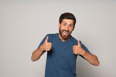 Handsome bearded man showing thumbs up on light grey background