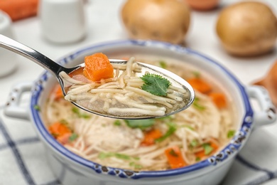 Spoon with fresh homemade chicken soup on table, closeup