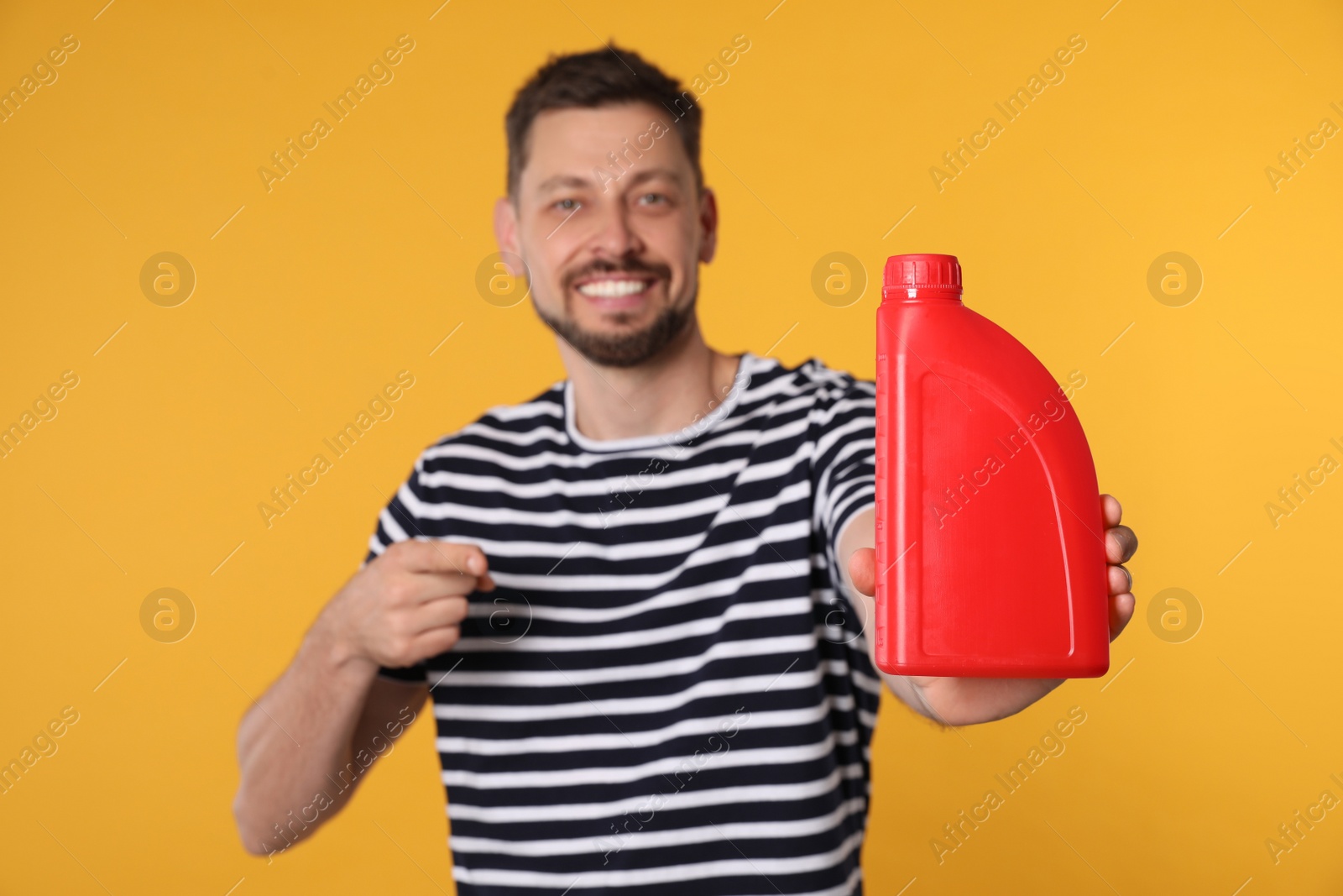 Photo of Man pointing at motor oil against orange background, focus on hand container