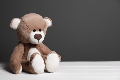 Cute teddy bear on white wooden table near black wall, space for text