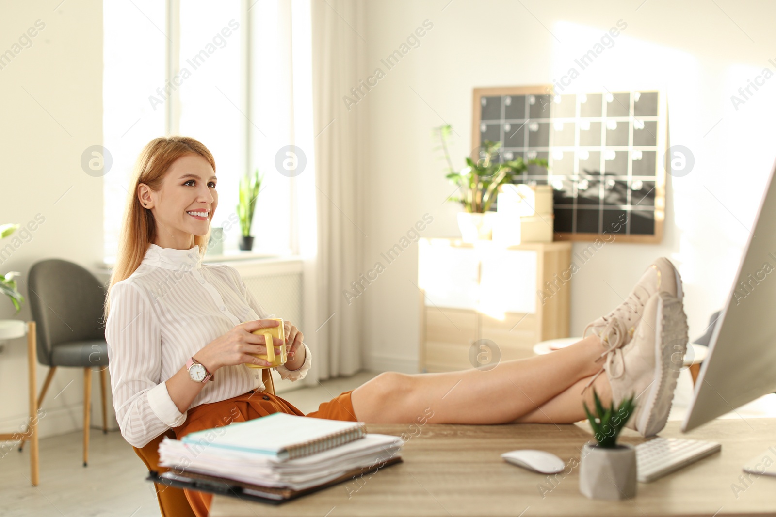 Photo of Young woman with cup of drink relaxing at table in office during break