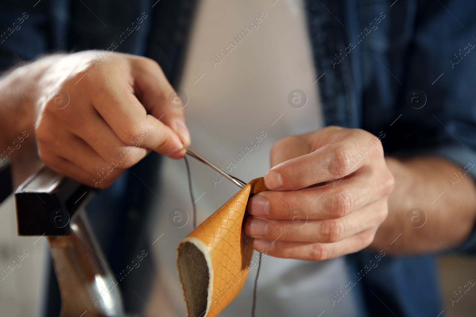 Photo of Man sewing piece of leather in workshop, closeup