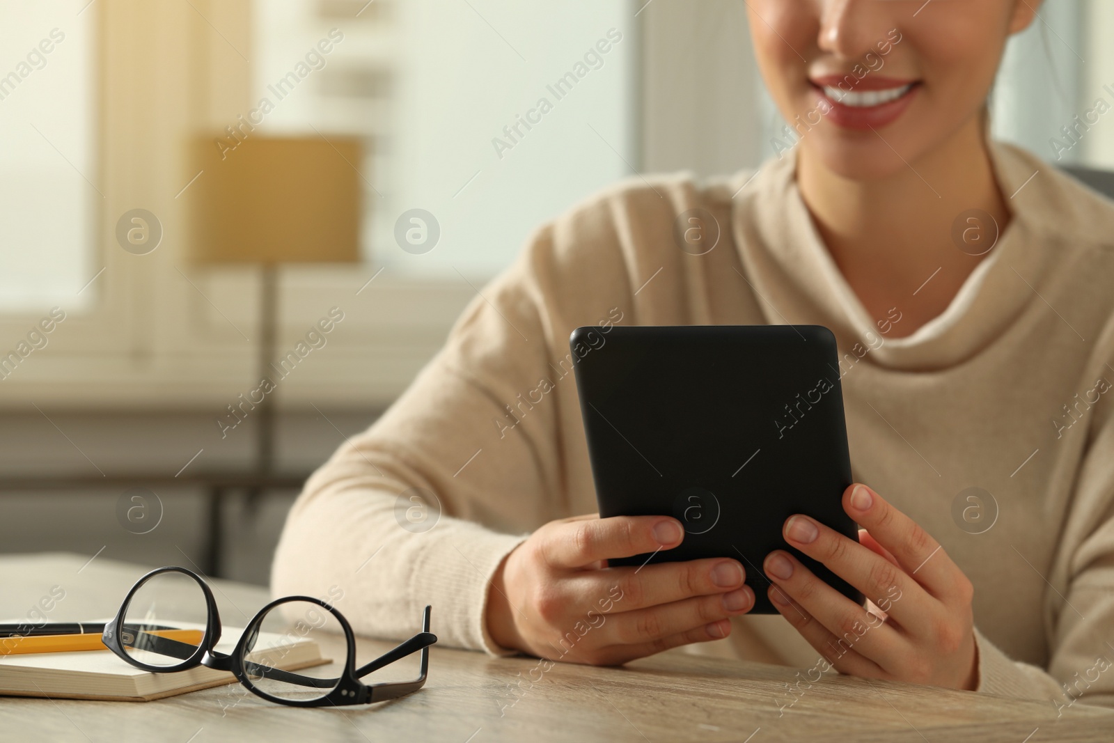 Photo of Young woman using e-book reader at wooden table indoors, closeup. Space for text