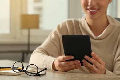 Photo of Young woman using e-book reader at wooden table indoors, closeup. Space for text