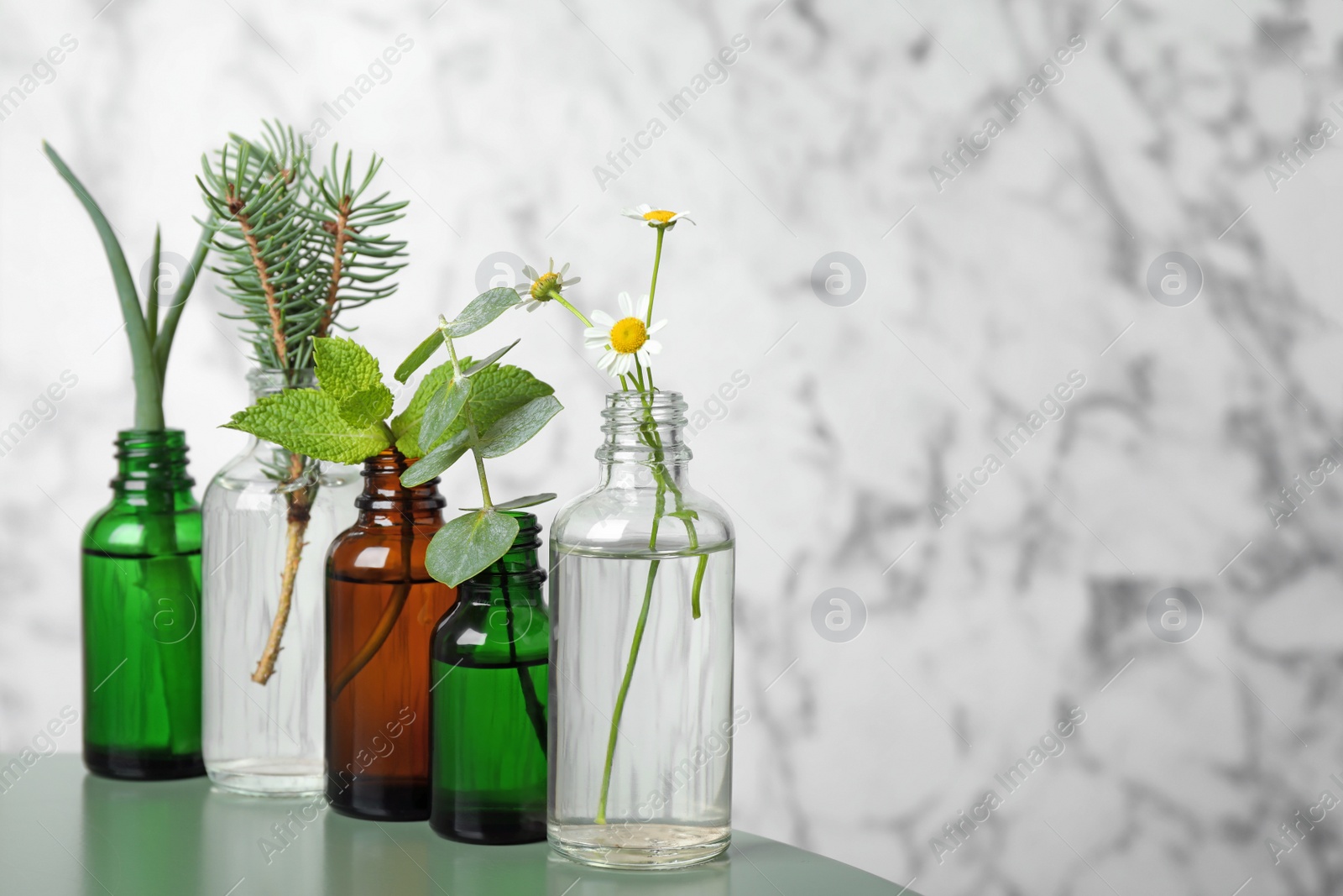 Photo of Glass bottles of different essential oils with plants on table. Space for text