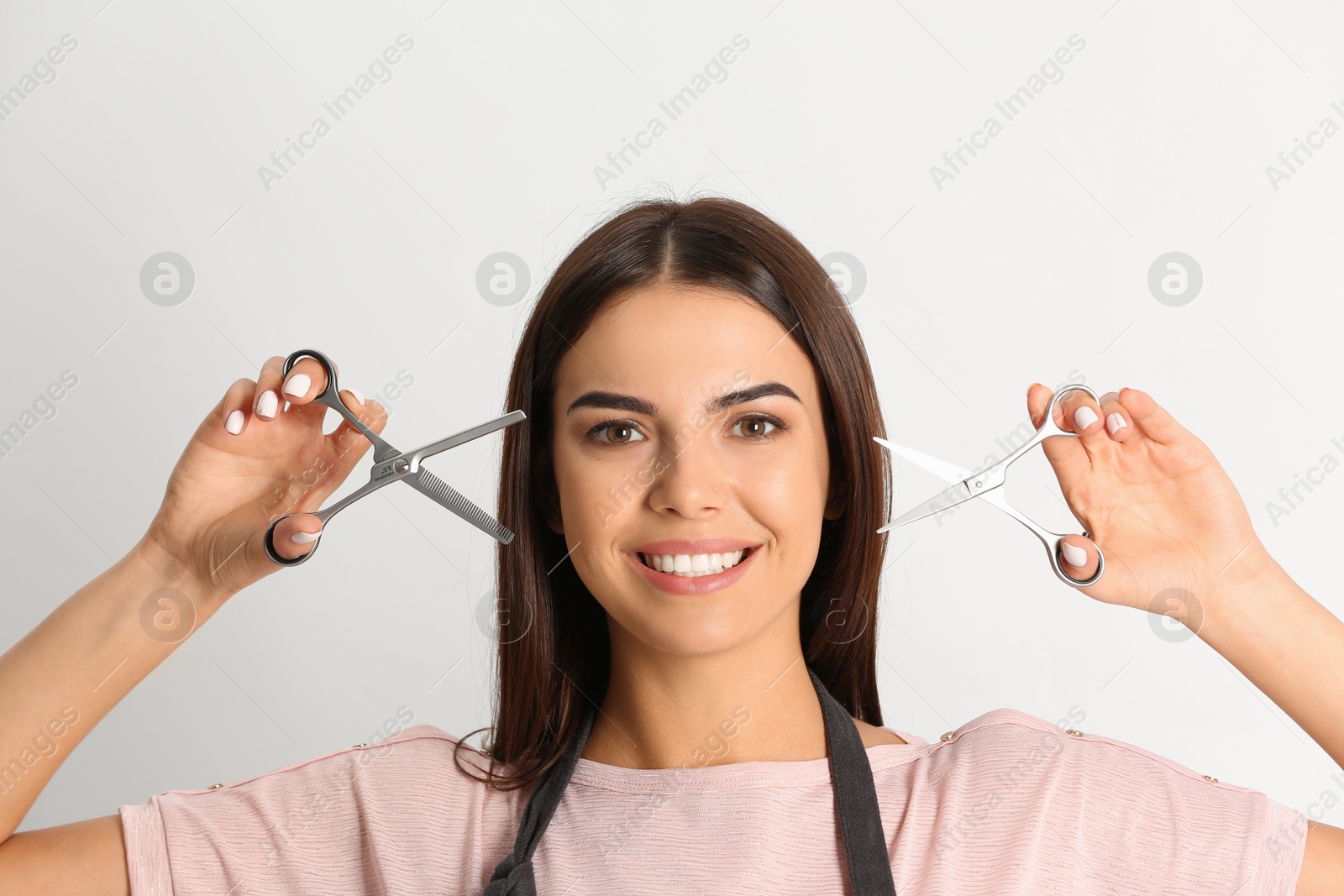 Photo of Young hairstylist holding professional scissors on light background