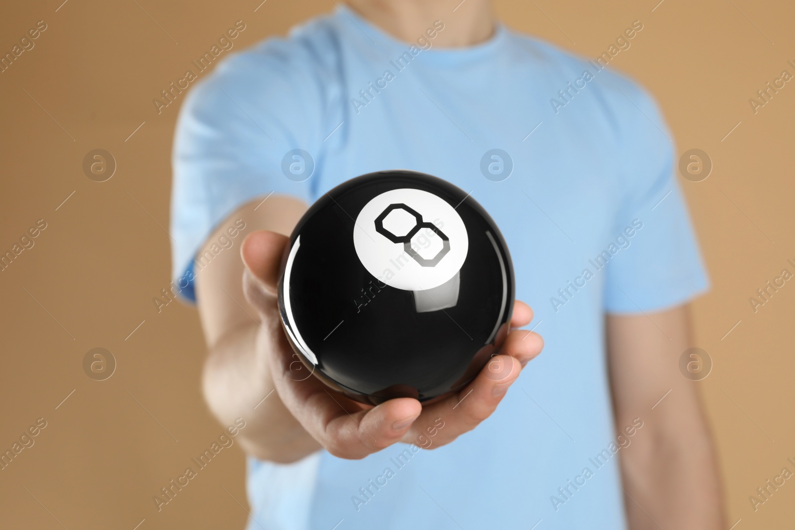 Photo of Man holding magic eight ball on light brown background, closeup