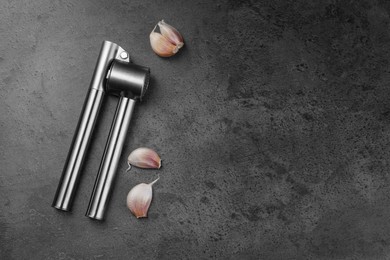 Photo of Garlic press and cloves on grey table, flat lay. Space for text
