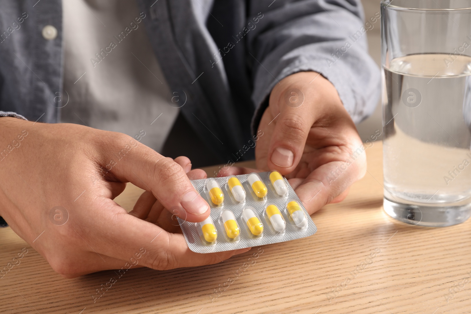 Photo of Man taking pill out from blister pack at wooden table, closeup