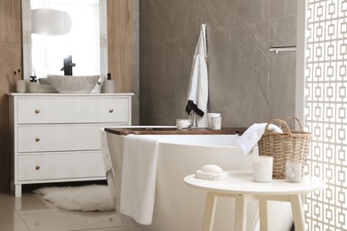 Photo of Modern white tub and table with toiletries in bathroom. Interior design