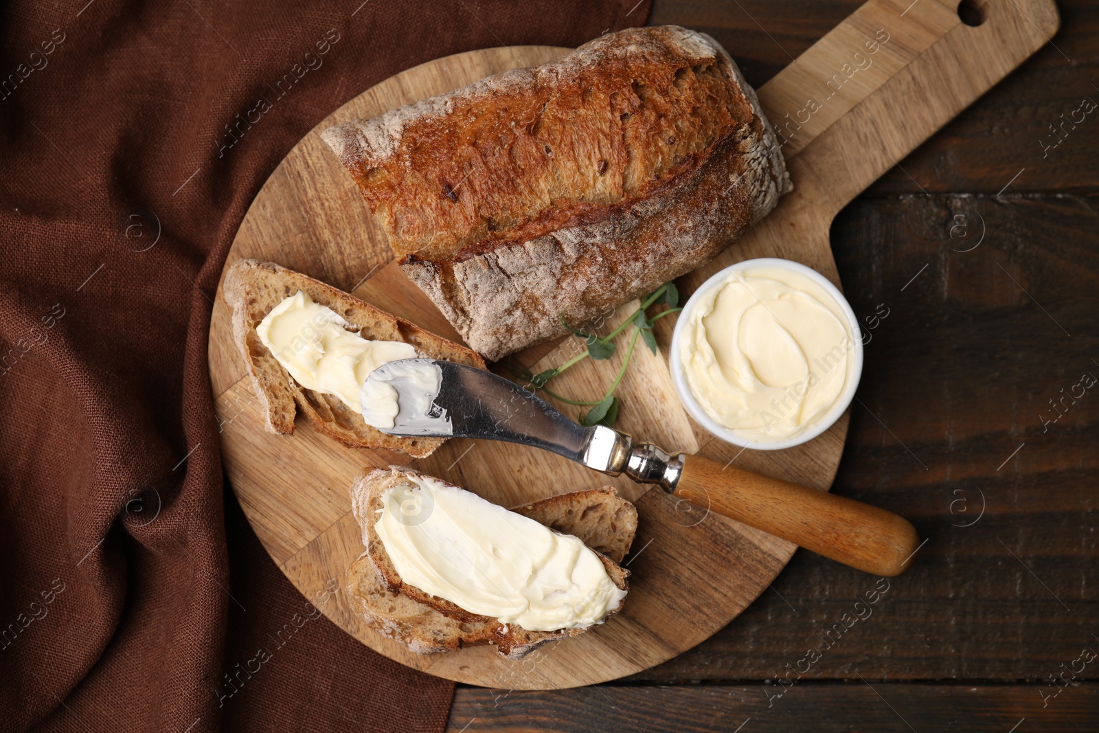 Photo of Tasty bread with butter and knife on wooden table, top view