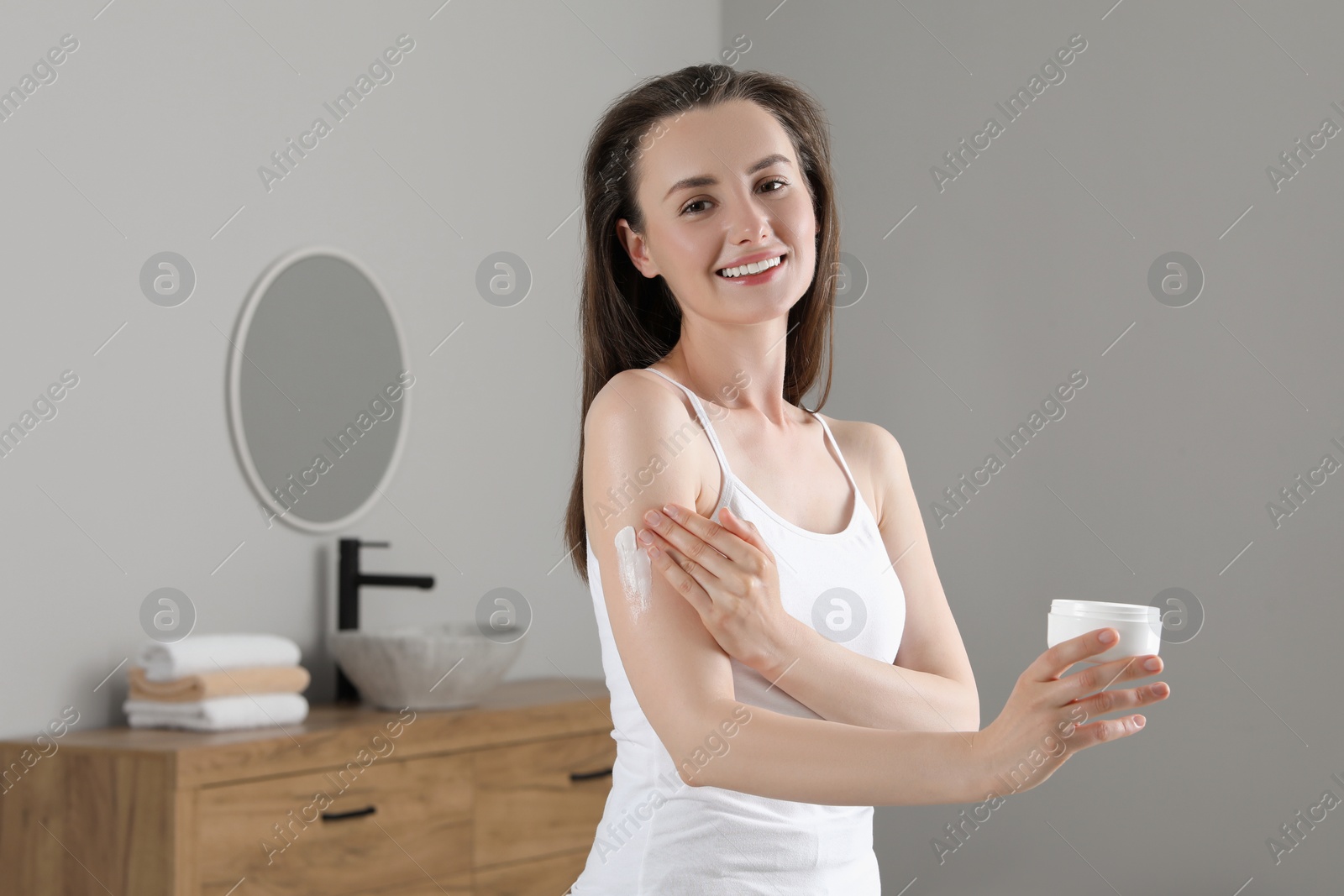 Photo of Happy woman applying body cream onto arm in bathroom, space for text