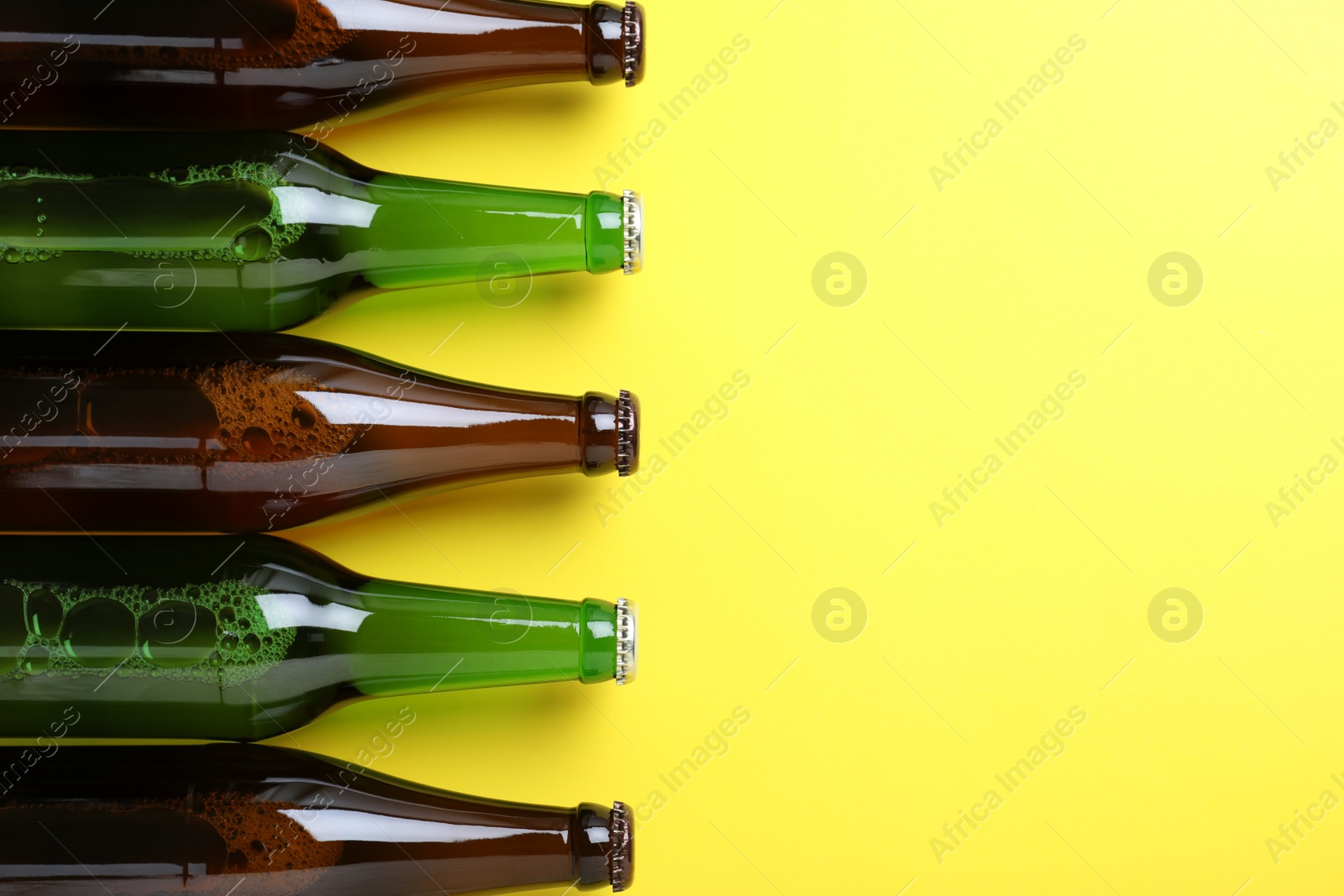 Photo of Bottles of beer on yellow background, flat lay. Space for text