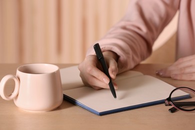 Photo of Woman writing in notebook at wooden table indoors, closeup