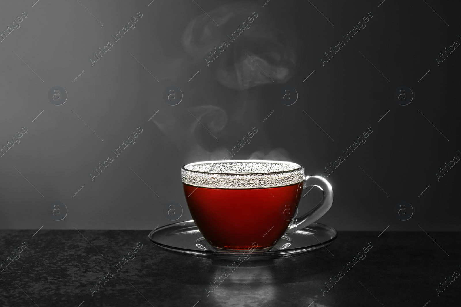 Photo of Glass cup of hot tea on stone table against grey background, space for text