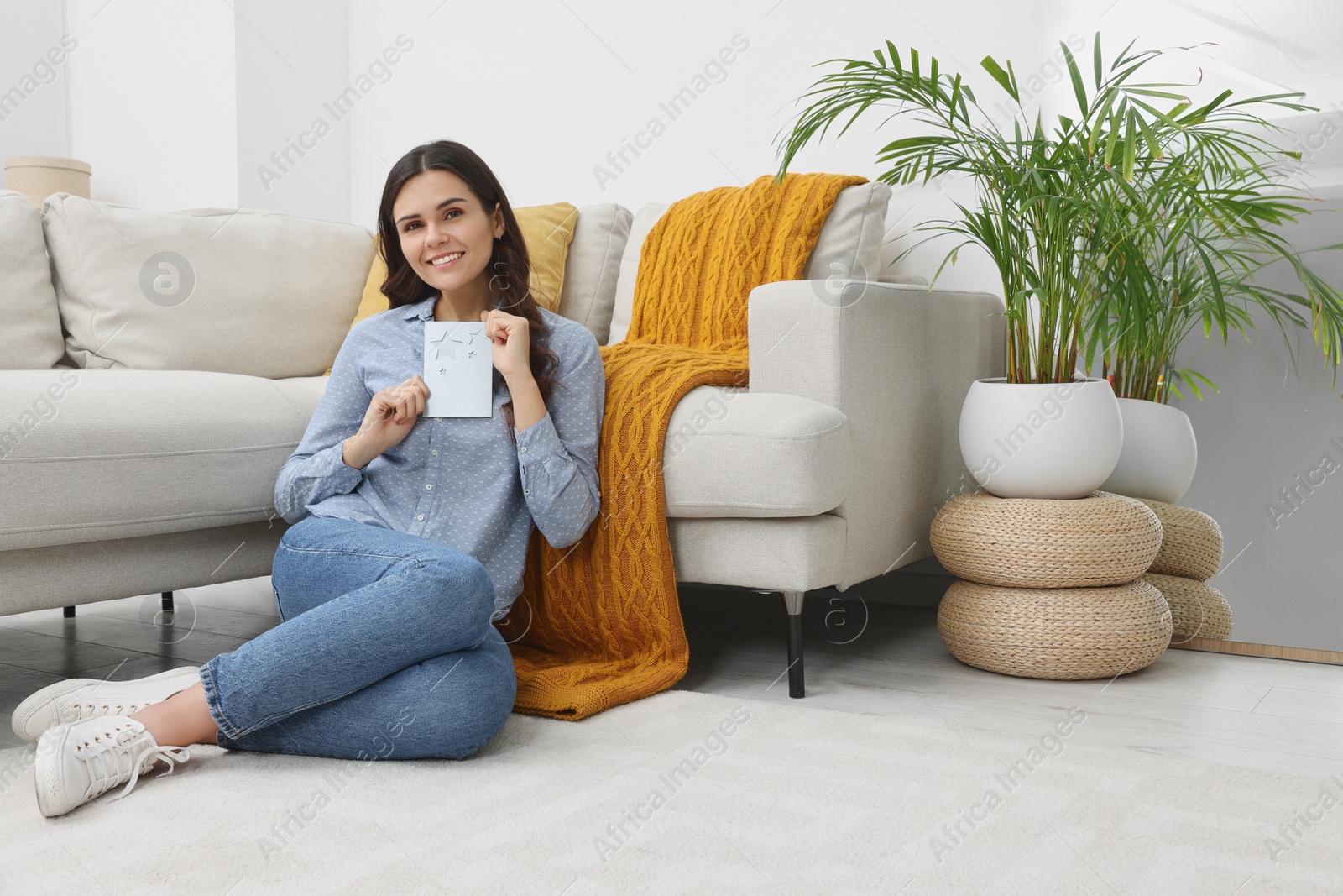 Photo of Young woman with greeting card on floor in living room