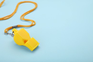 One yellow whistle with cord on light blue background. Space for text