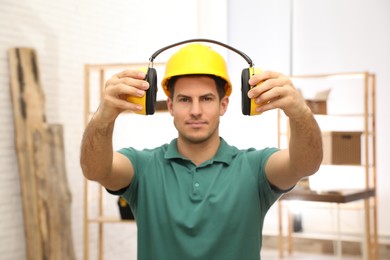 Photo of Worker holding safety headphones indoors, focus on hands. Hearing protection device