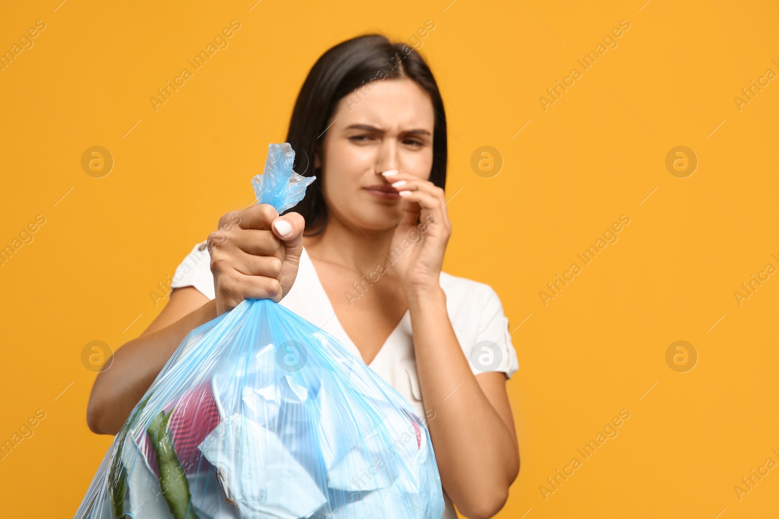 Photo of Woman holding full garbage bag against yellow background, focus on hand