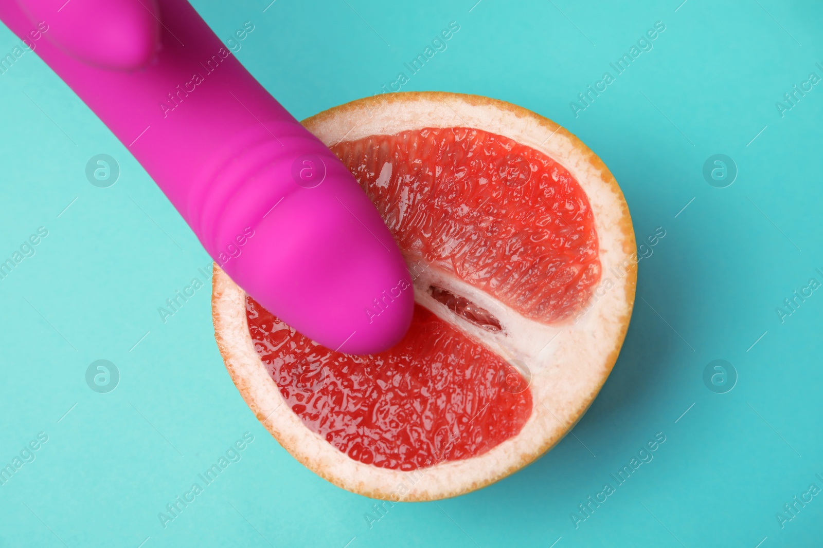 Photo of Half of grapefruit and purple vibrator on turquoise background, flat lay. Sex concept