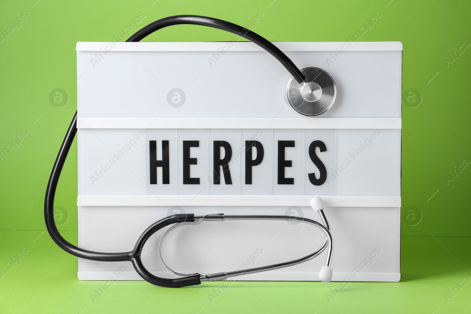 Photo of Light box with word Herpes and stethoscope on green background