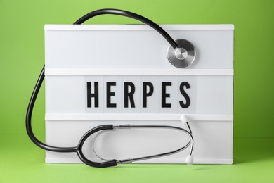 Photo of Light box with word Herpes and stethoscope on green background