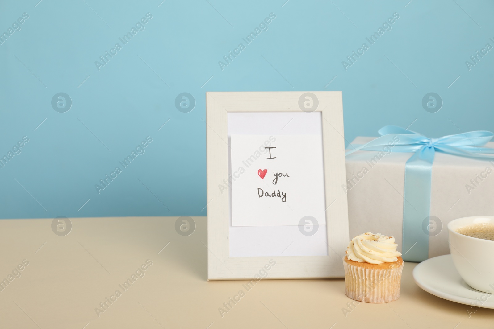 Photo of Happy Father's Day. Tasty cupcake, cup, card with phrase I Love You, Daddy in frame and gift box on beige table, closeup. Space for text