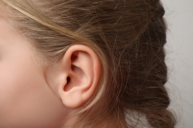 Photo of Closeup view of little girl against light gray background, focus on ear