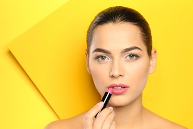 Photo of Young woman applying lipstick on color background