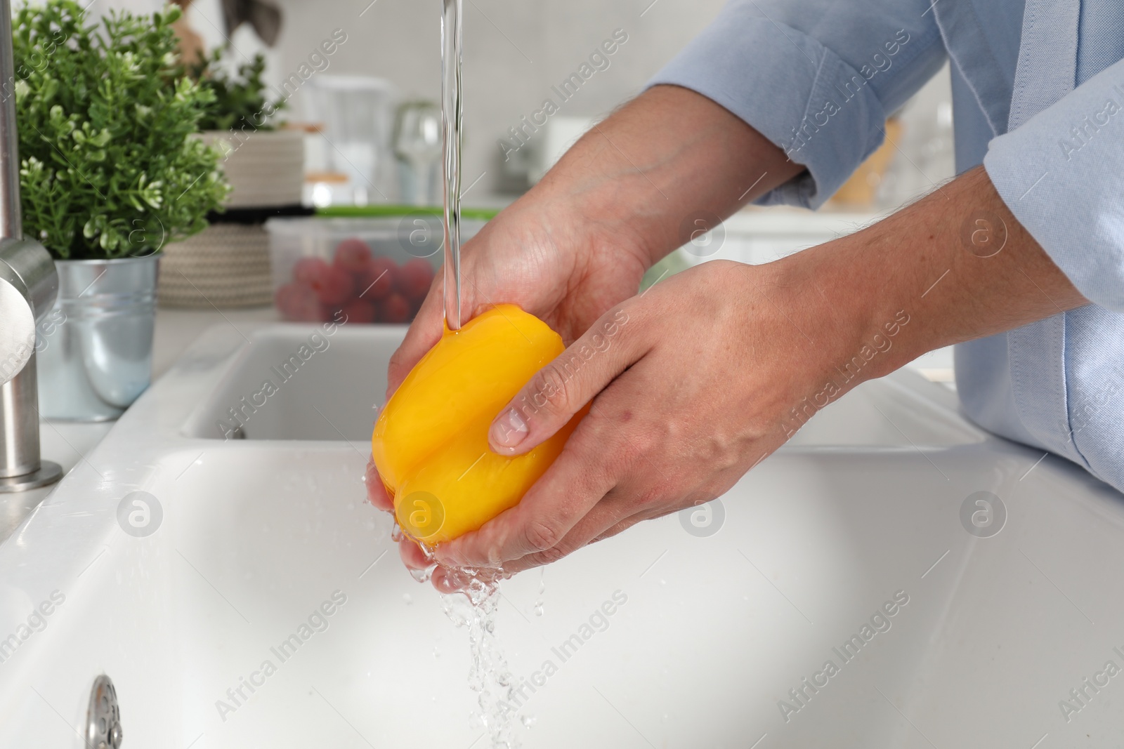 Photo of Man washing fresh bell pepper in kitchen, closeup