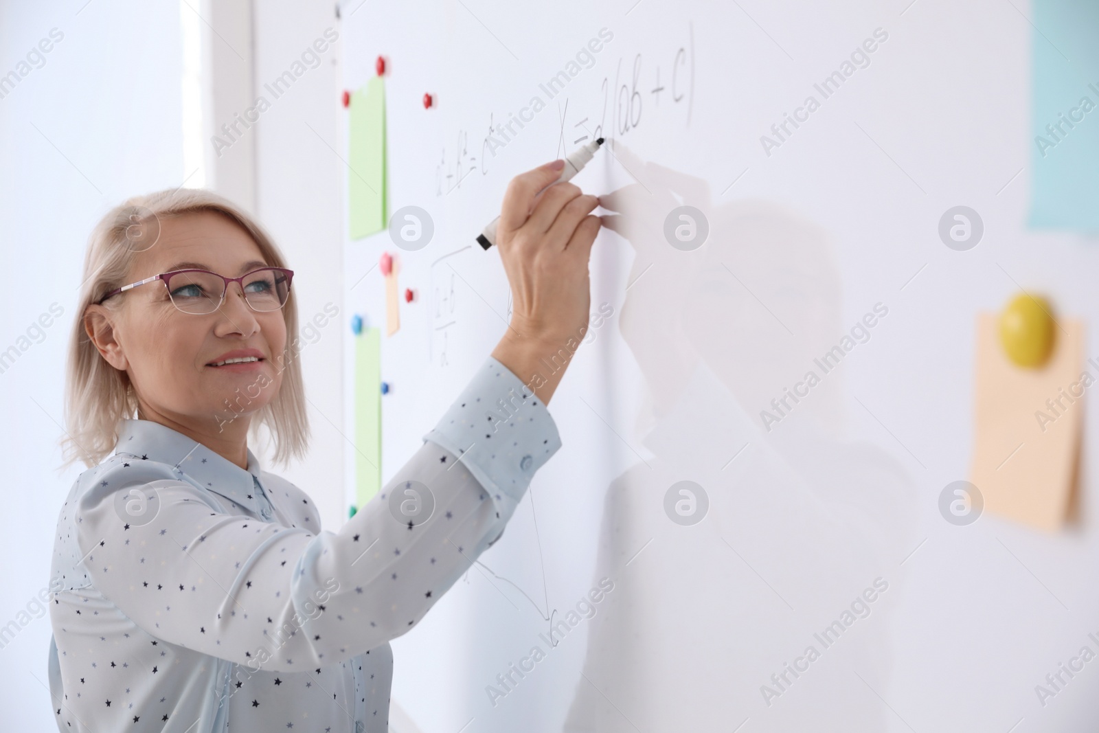 Photo of Mature teacher writing on whiteboard in modern classroom