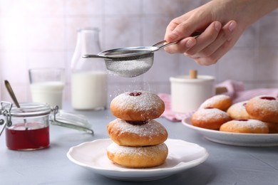 Photo of Woman dusting powdered sugar onto delicious Hanukkah donuts on light grey table, closeup
