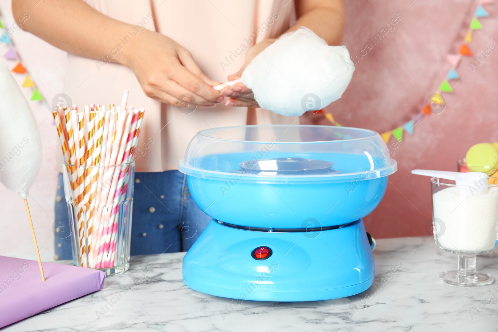 Photo of Woman making cotton candy using modern machine at table, closeup