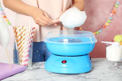 Woman making cotton candy using modern machine at table, closeup