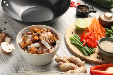 Different products and wok on light wooden table, closeup