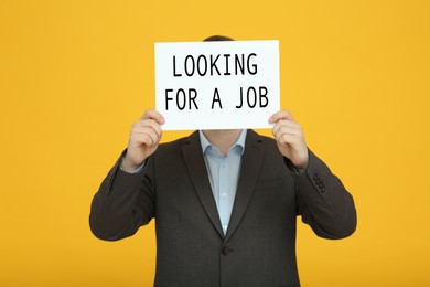 Photo of Unemployed man holding sign with phrase Looking For A Job on orange background