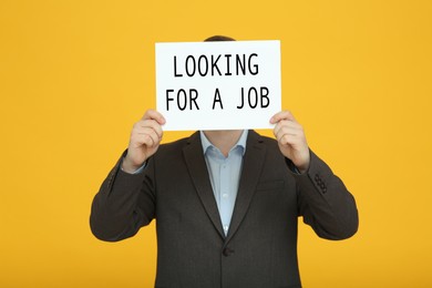 Unemployed man holding sign with phrase Looking For A Job on orange background