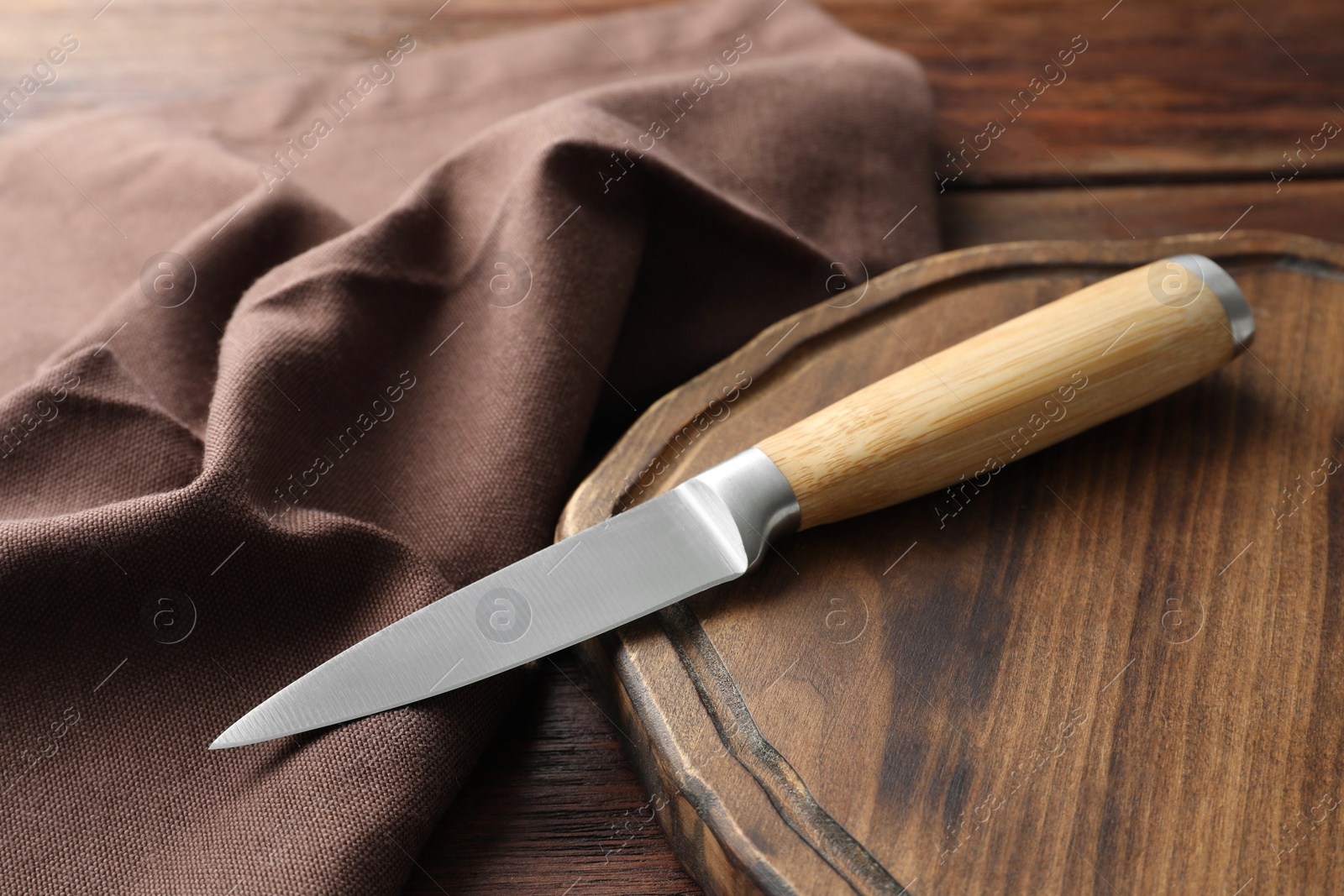 Photo of One sharp knife, cloth and board on wooden table, closeup