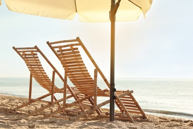Photo of Wooden deck chairs and outdoor umbrella on sandy beach. Summer vacation
