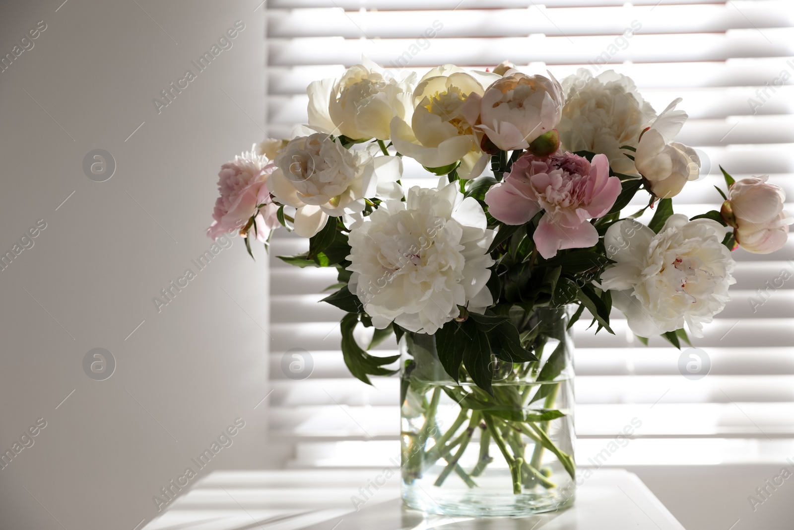 Photo of Beautiful peonies in vase on table near window indoors