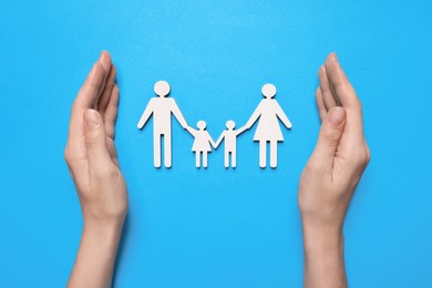 Photo of Woman protecting figures of family on light blue background, top view. Insurance concept