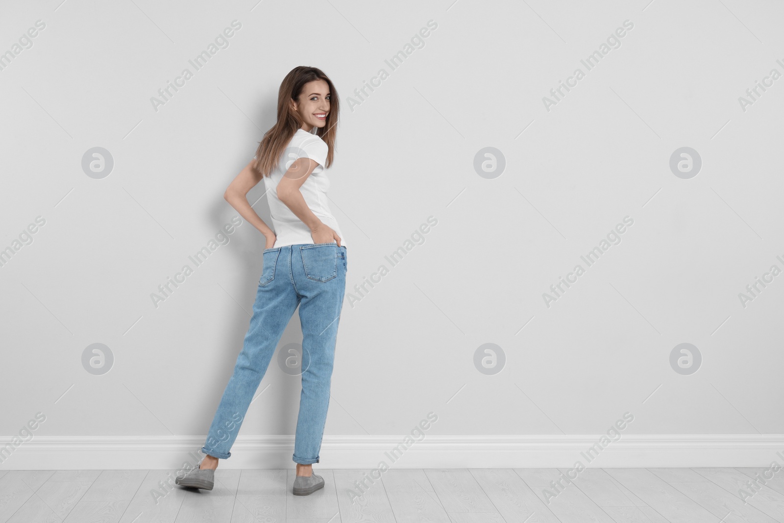 Photo of Young woman in stylish jeans near light wall. Space for text